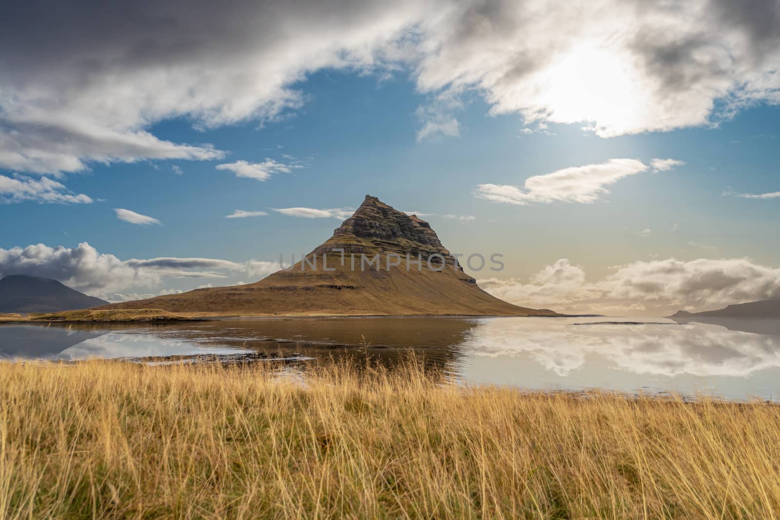 Kirkjufell reflecting in calm lake during sunny weather in Iceland Snaefellsness National Park