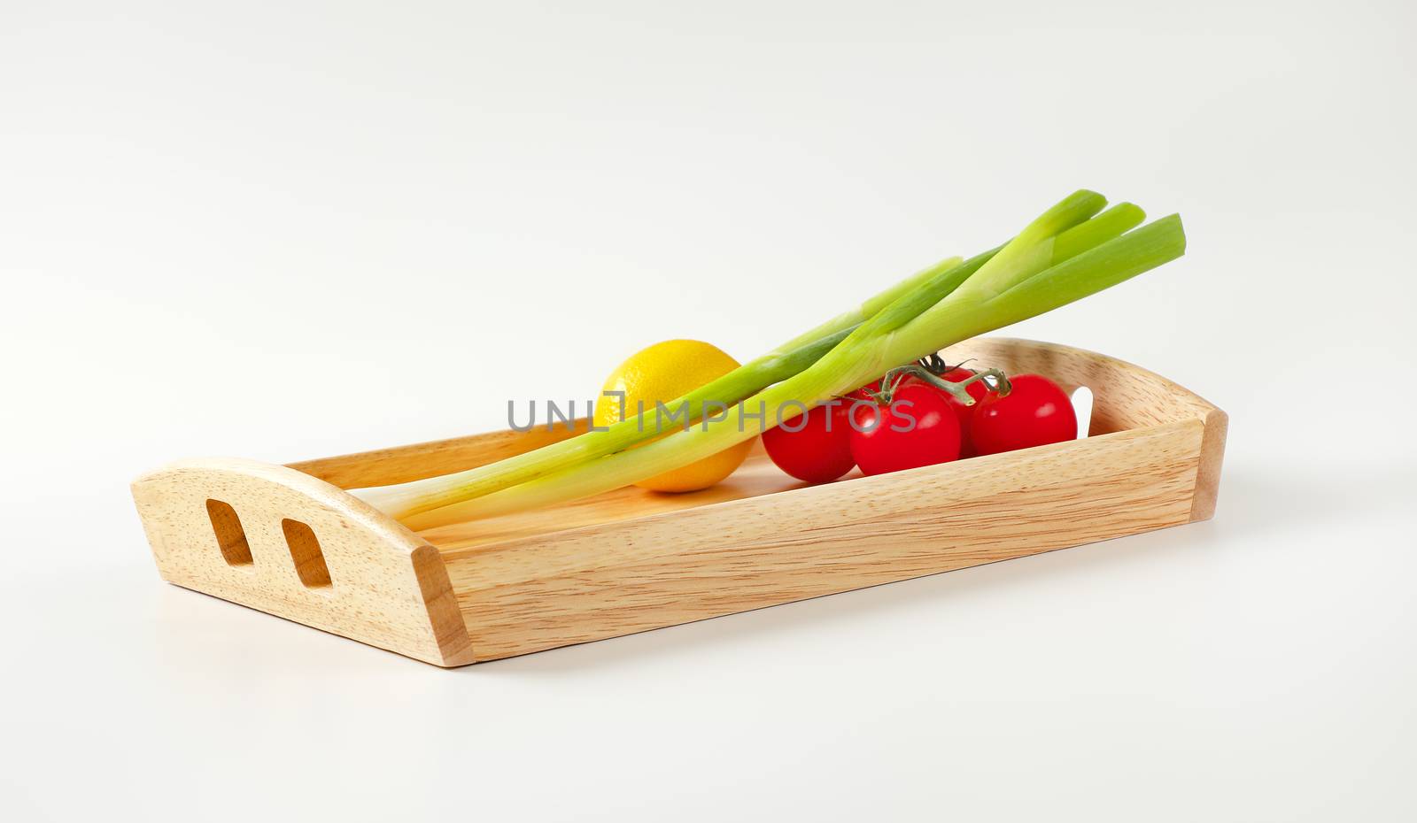Spring onion, tomatoes and lemon on wooden serving tray