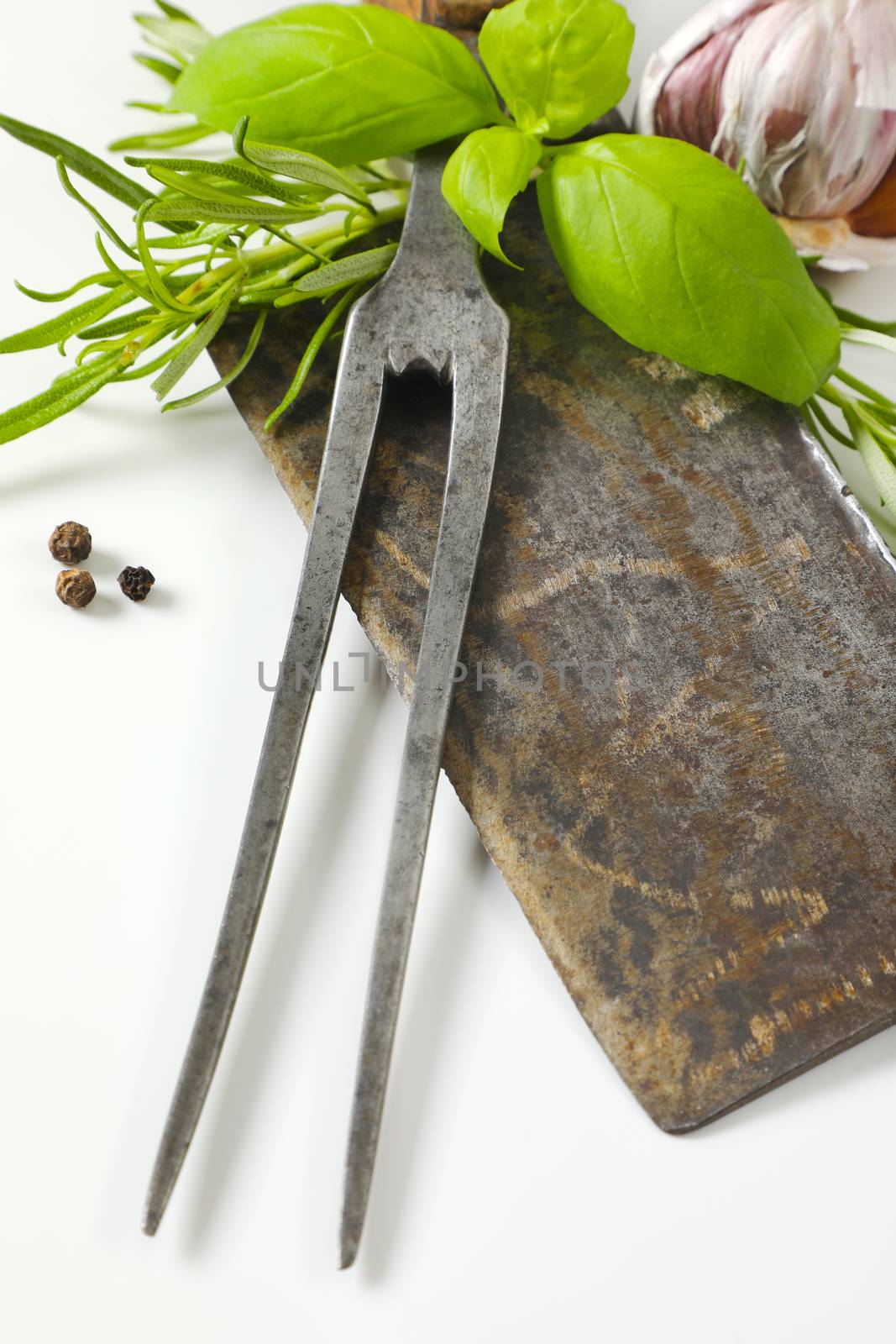 Vintage meat cleaver knife, carving fork, fresh culinary herbs, garlic and peppercorns