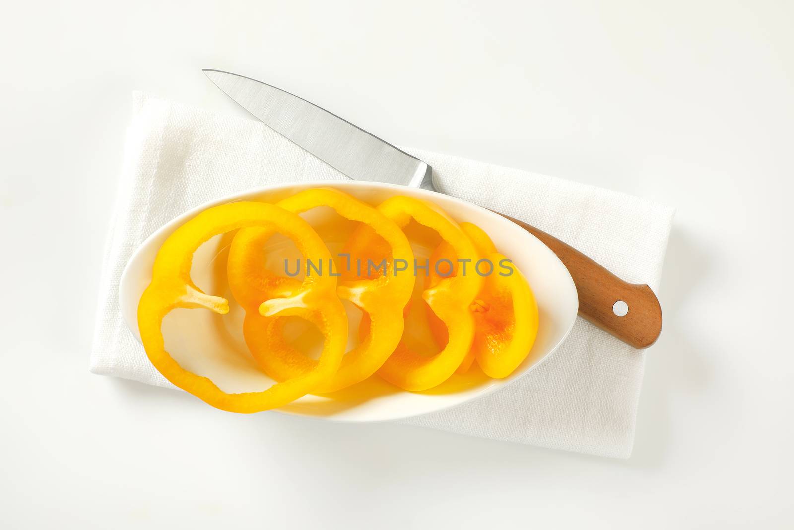 Sliced yellow bell pepper in white bowl and kitchen knife next to it