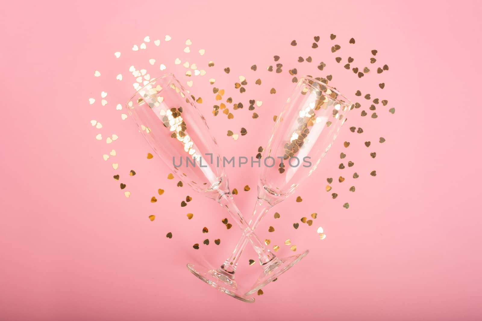 Valentines day champagne flutes glasses and heart shaped golden glitters on pink background with copy space for text