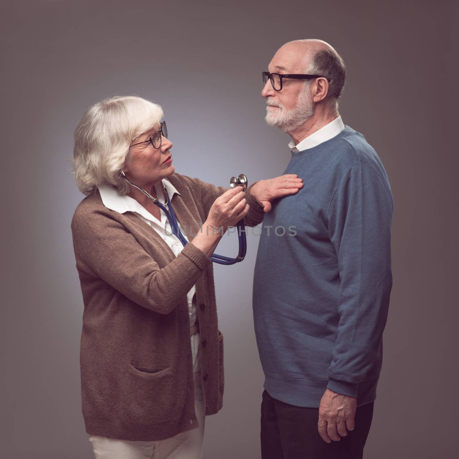 Senior woman taking care of husband, checking heart beat with stethoscope