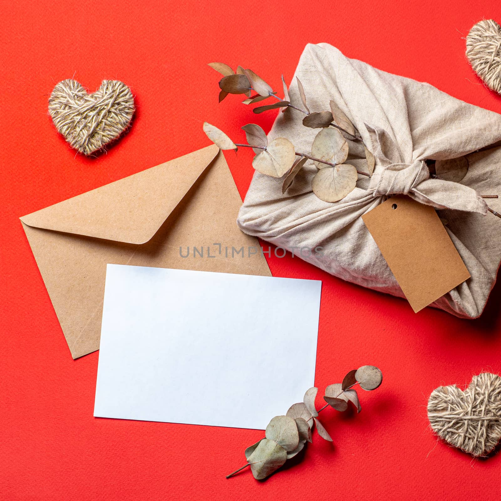 Zero waste Valentine's Day concept and mock up on red. Eco-friendly gift cloth wrapping in Furoshiki style, craft paper envelope,empty greetings card. Top down view or flat lay. Copy space for design