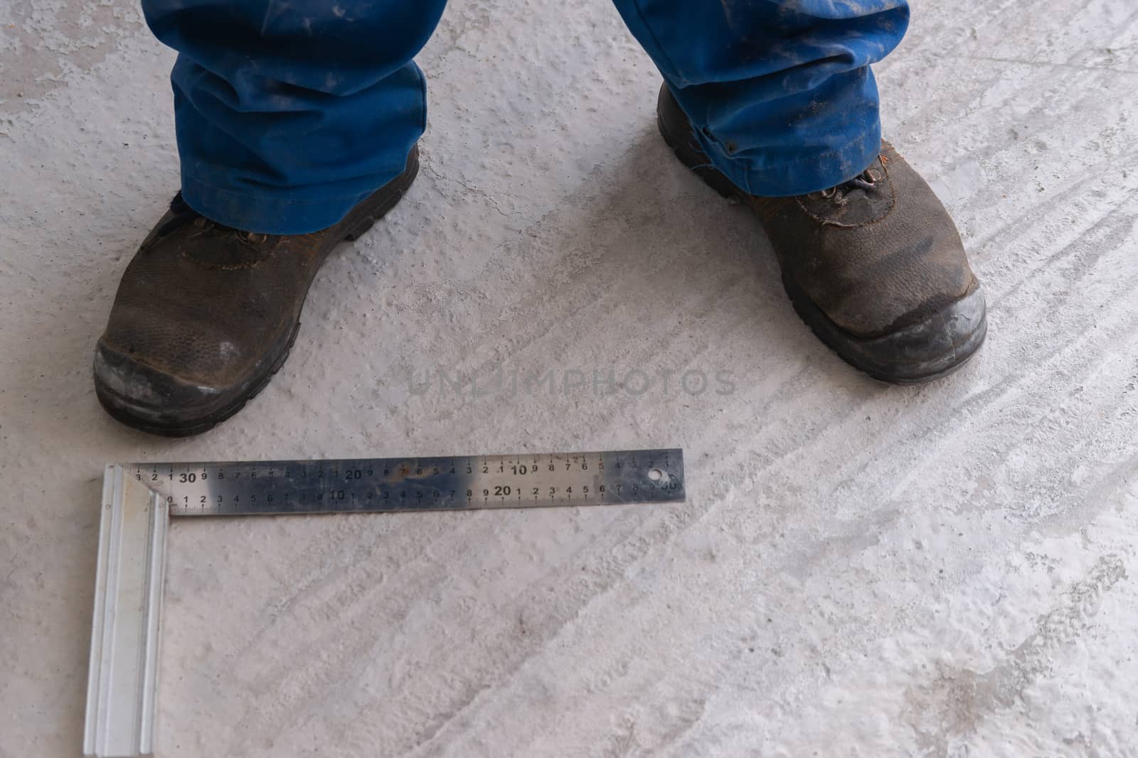 A man is standing on a concrete floor unfinished construction near ruler, measuring tape and metal setsquare.