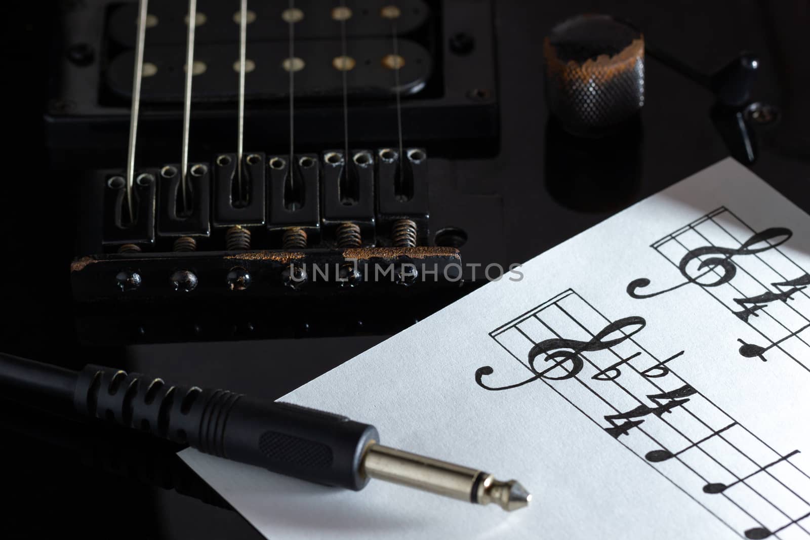 Music note and jack cable on black electric guitar in darkness. Concept of rock music creative.