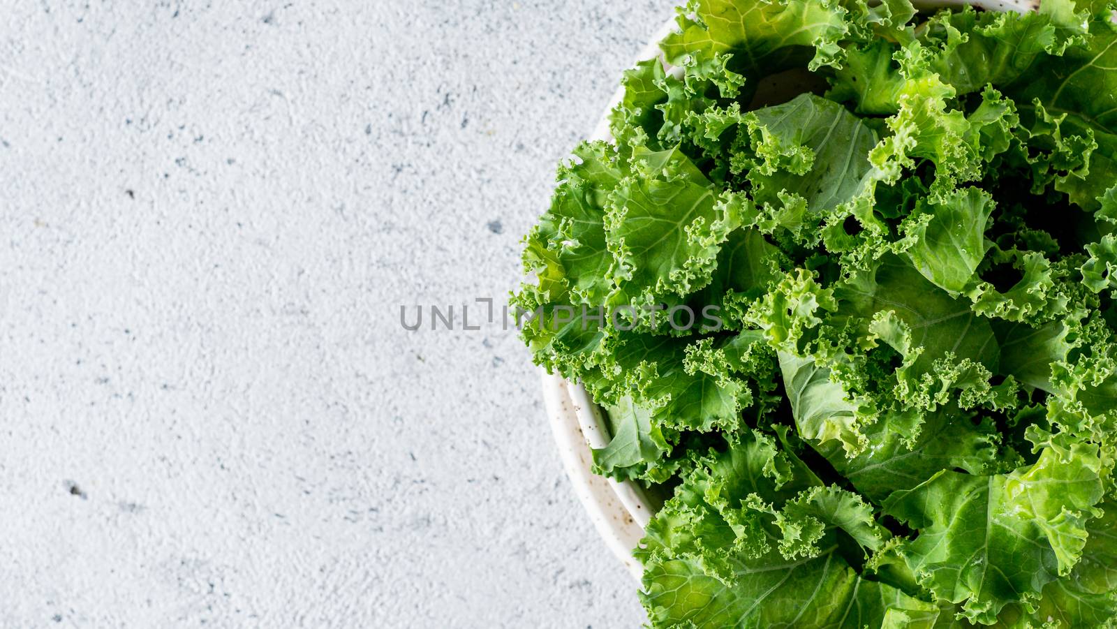 Kale close up. Green vegetable leaves, top view in white craft bowl over gray cement background. Healthy eating, vegetarian food,dieting concept. Top view or flat lay. Copy space. Health kale benefits