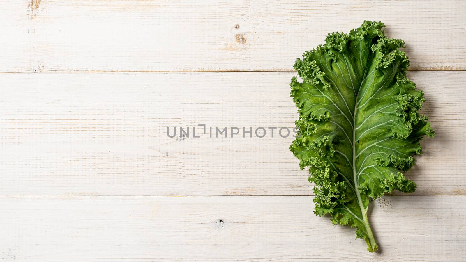 Fresh green kale leaf on white wooden tabletop, copy space left. Flat lay or top view. Healthy detox vegetables. Clean eating and dieting concept. Health kale benefits. Banner