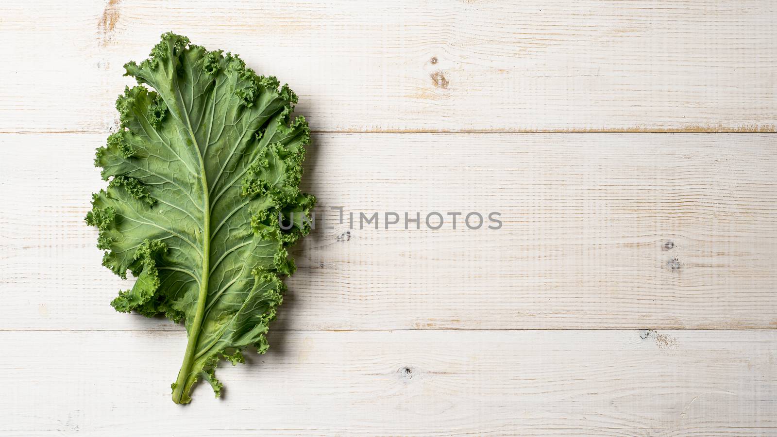 Green kale leaf on white wood table, copy space, top view by fascinadora