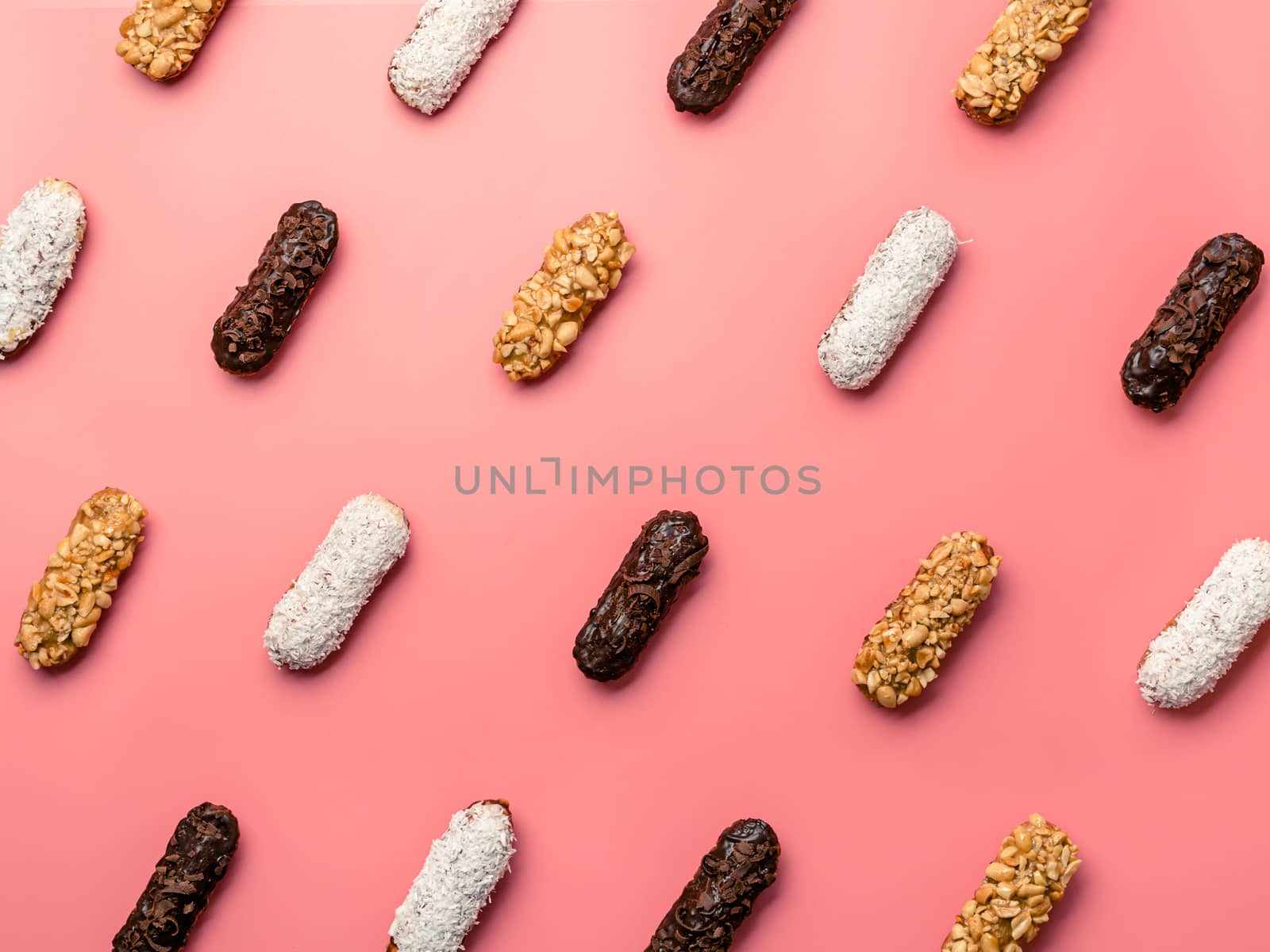 Pattern of different homemade eclairs on pink background. Top view of delicious healthy profitroles with different decor - chocolate, peanut and sherdded coconut