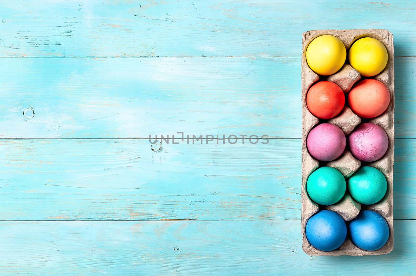Easter concept. Colorful eggs in cardboard packaging on blue wooden background with copy space for text. Top down view or flat lay