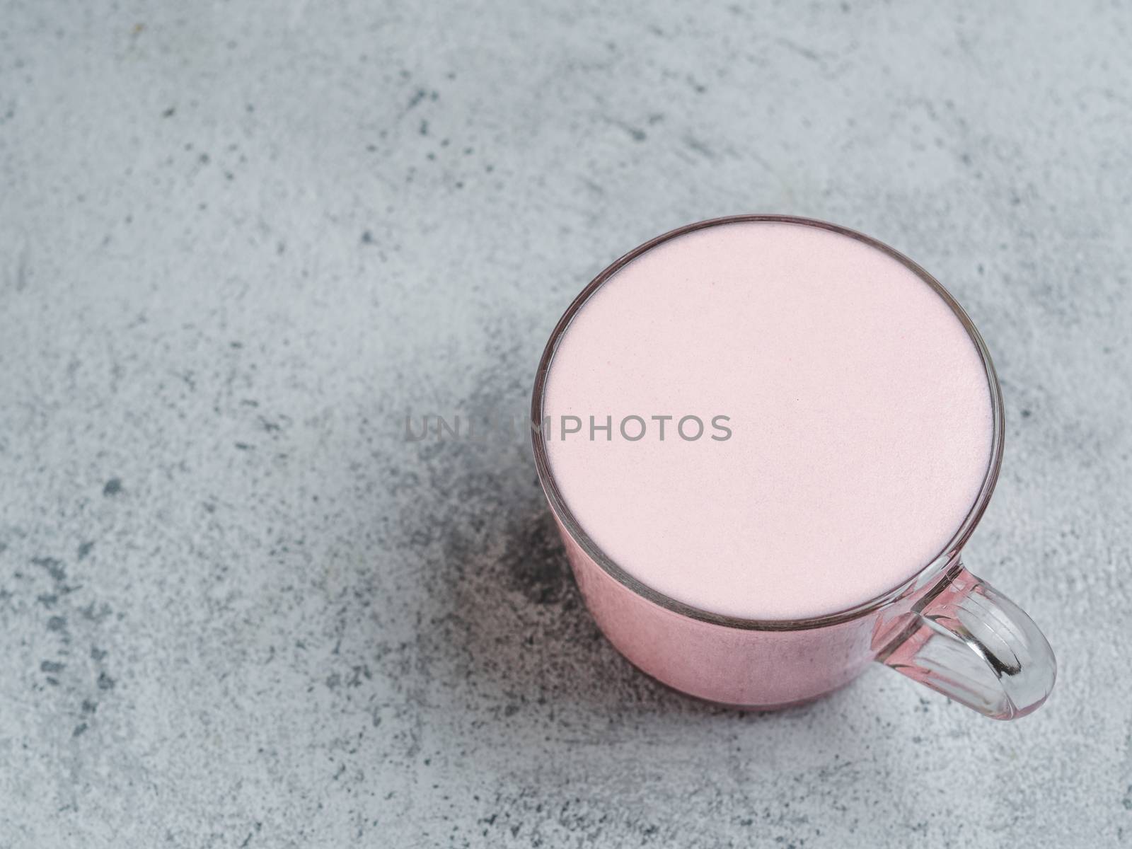 Trendy drink: pink latte. Beetroot or raspberries cappuccino or latte in glass cup on gray cement background. Copy space for text.