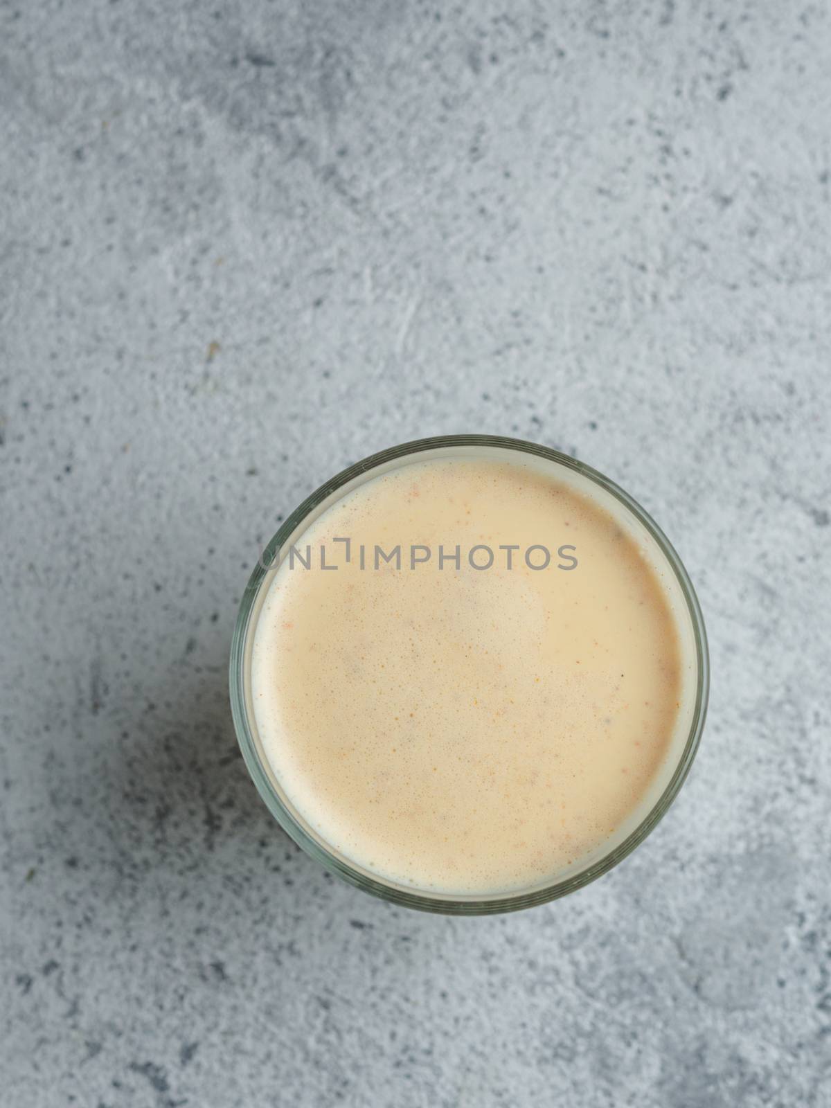 Healthy drink golden turmeric latte in glass cup. Yellow homemade latte on gray background. Detox turmeric tea latte. Copyspace for text Top view or flat lay. Vertical.