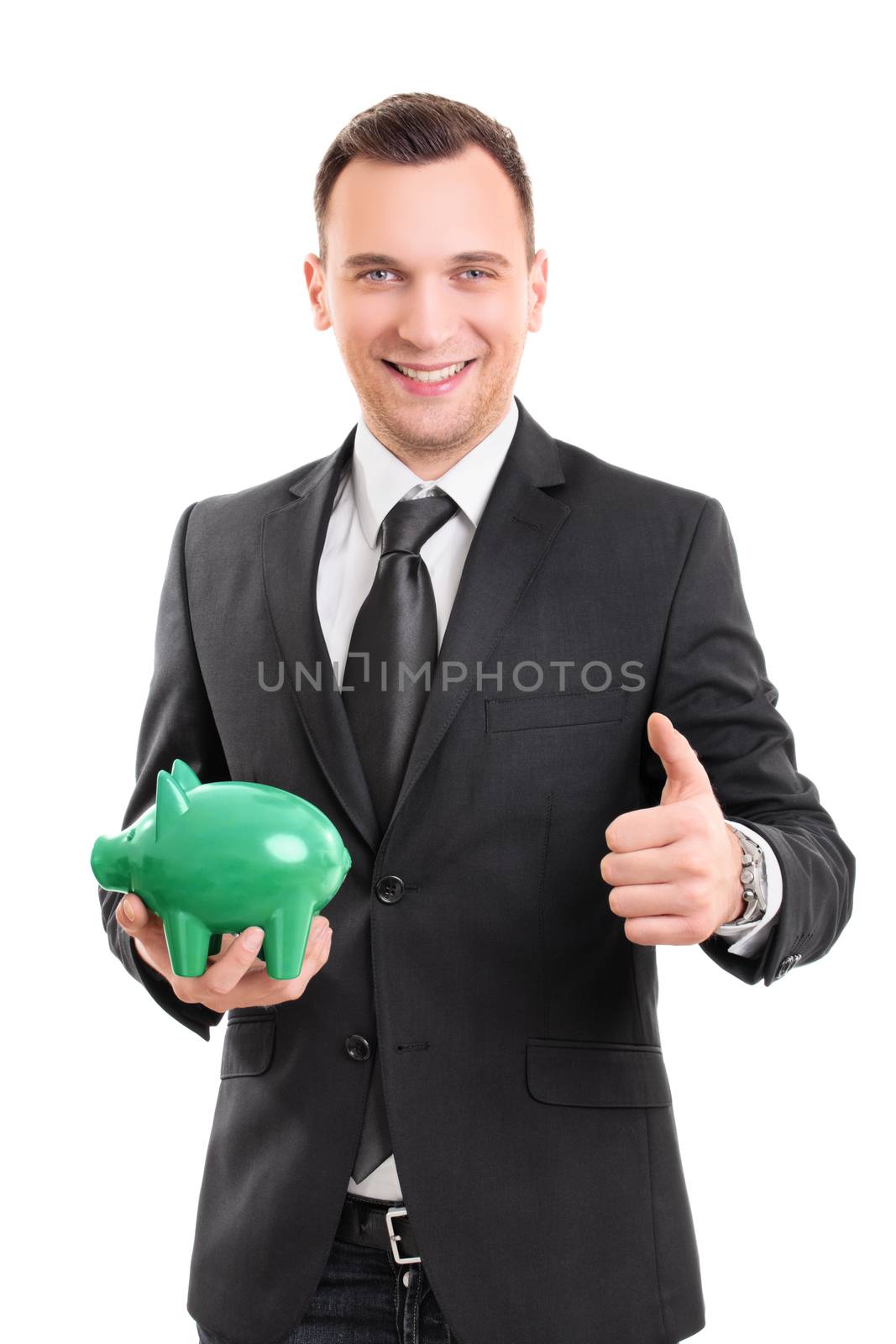 Handsome young businessman in a suit holding a piggy bank, smiling and giving thumb up, isolated on white background. Saving money concept. Confident businessman with a piggy bank.