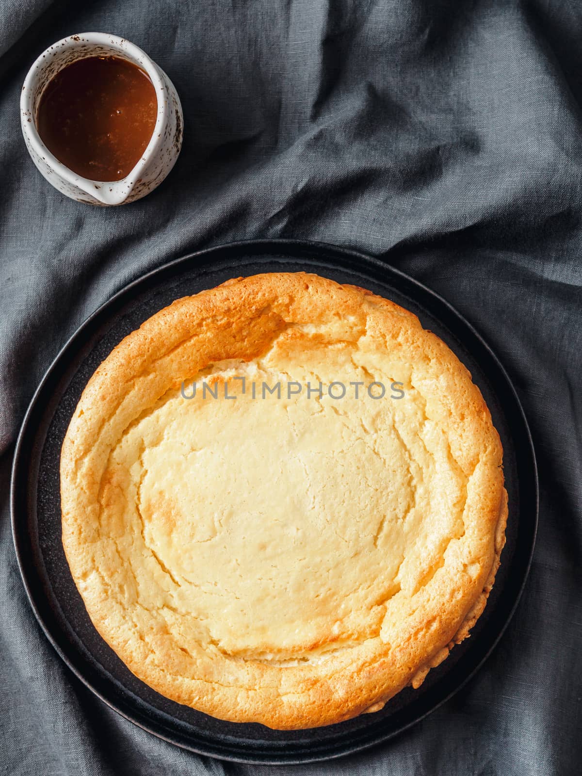 Plate with whole cheesecake pie on table with tablecloth. Classic cheesecake, caramel and dessert forks. Vertical. Top view or flat lay.