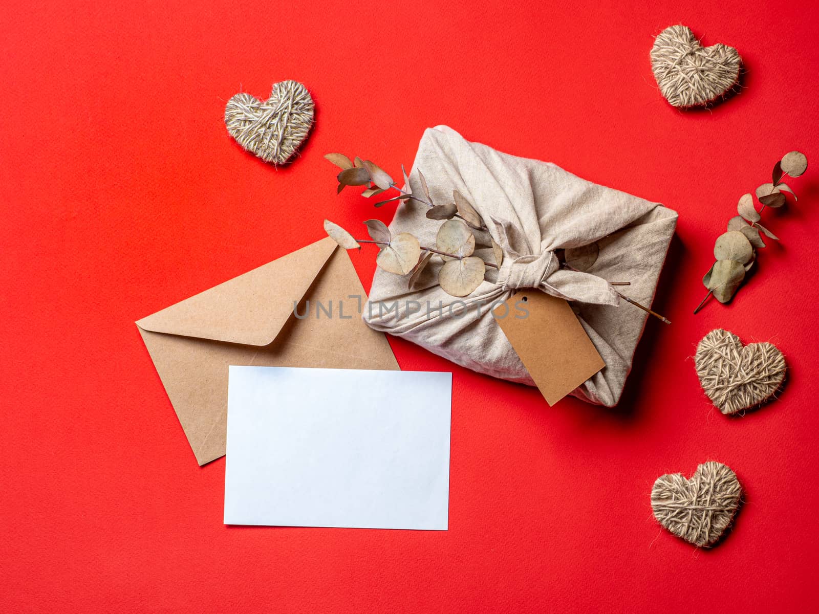 Zero waste Valentine's Day concept and mock up on red. Eco-friendly gift cloth wrapping in Furoshiki style, craft paper envelope,empty greetings card. Top down view or flat lay. Copy space for design