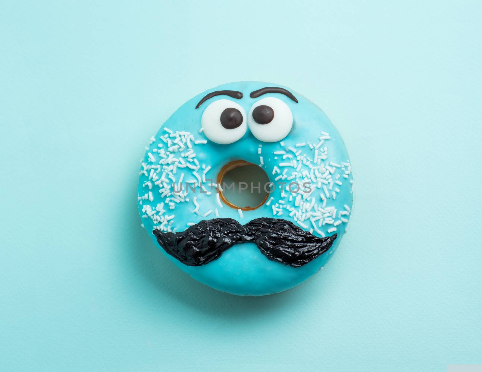 Blue glazed donut with mustache. Blue doughnut with funny face with mustache on blue background. Copy space for text. Masculinity or father day concept. Top view or flat lay