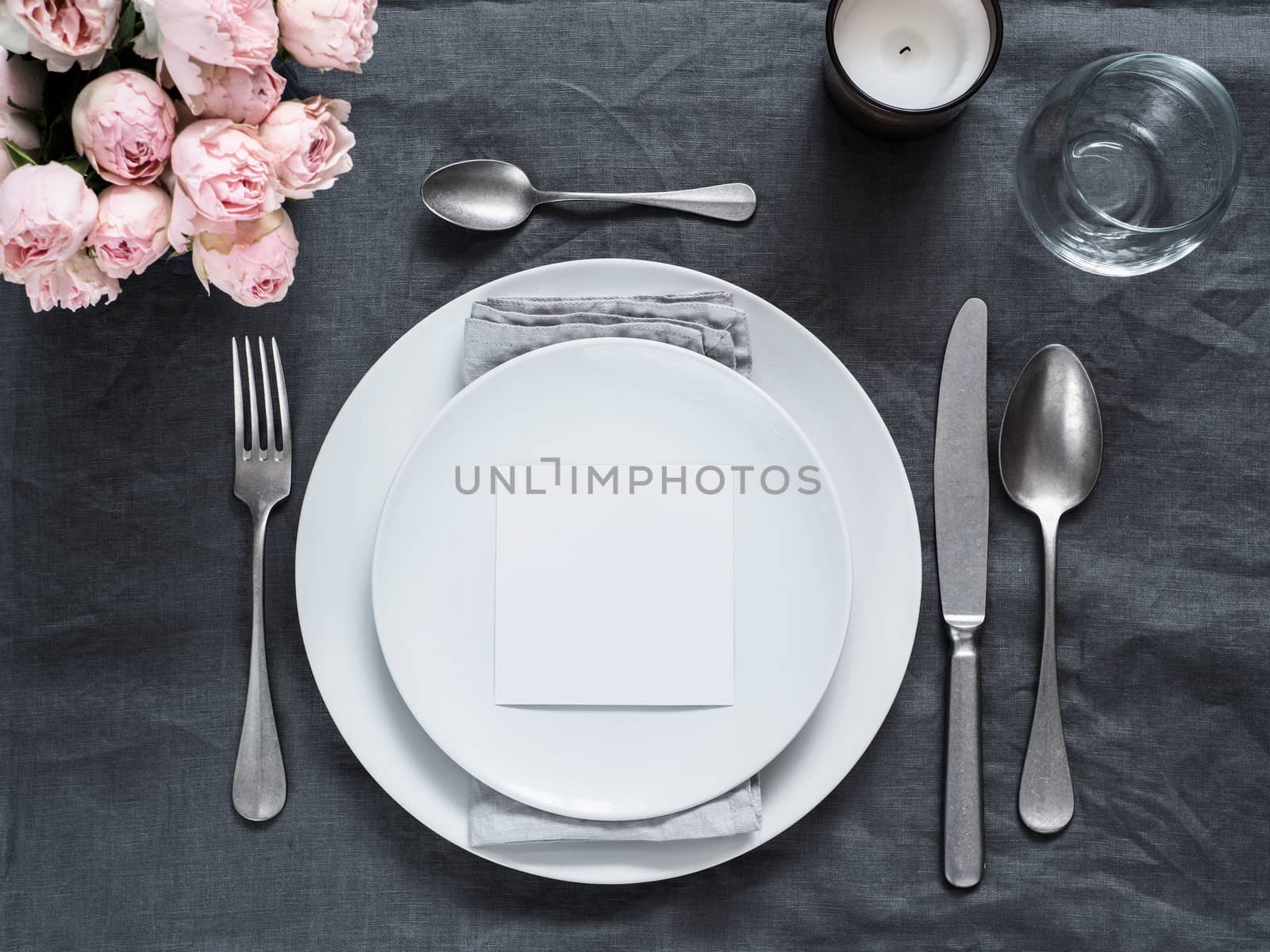 Menu, wedding invitation mock up. Beautiful table setting on gray linen tablecloth. Festive table setting for wedding dinner with pink spray roses and cabdle. Holiday dinner, white plates. Copy space