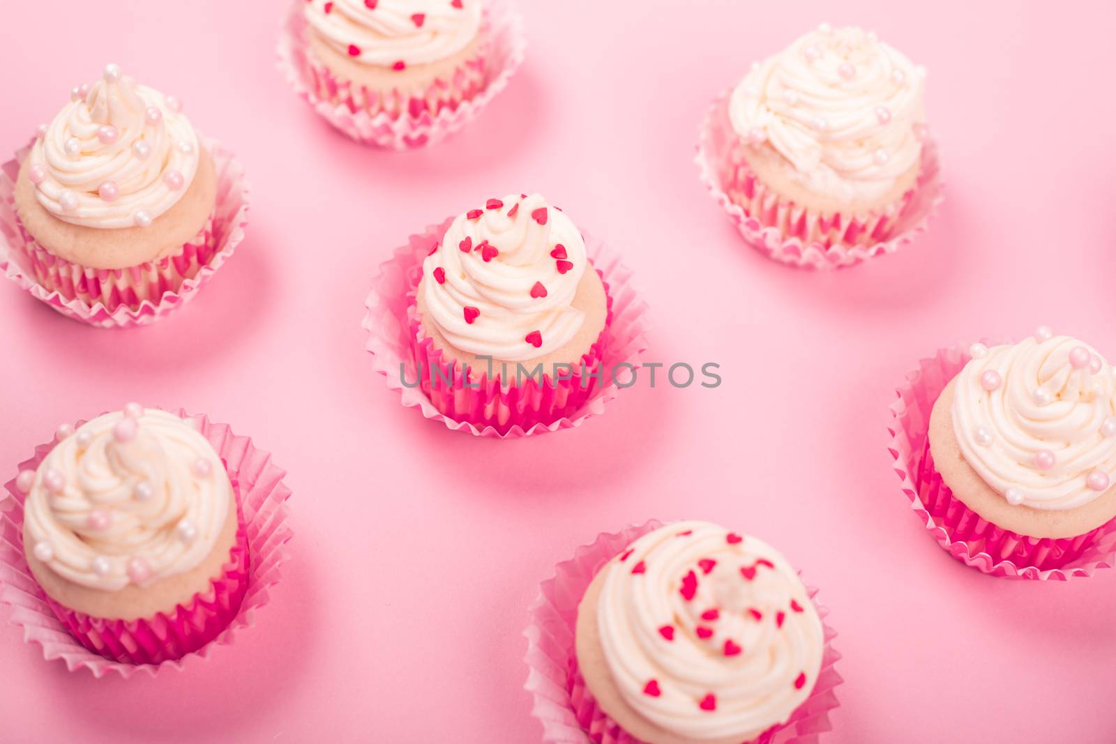 Valentine day love cupcakes decorated with cream and hearts on pink background