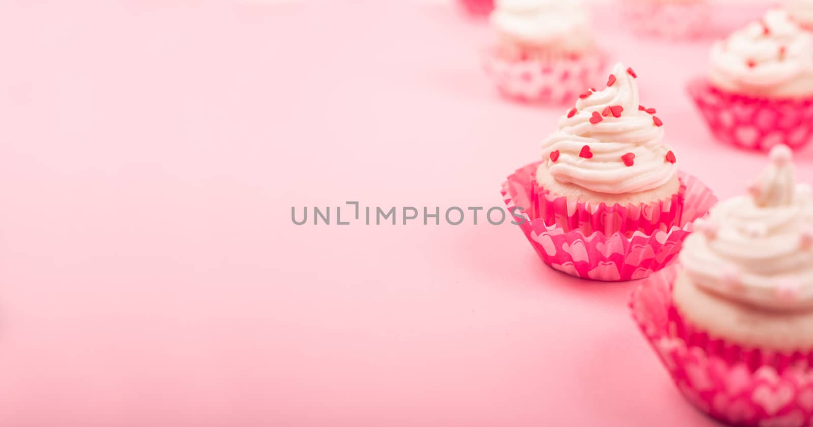 Valentine day love cupcakes decorated with cream and hearts on pink background with copy space for text