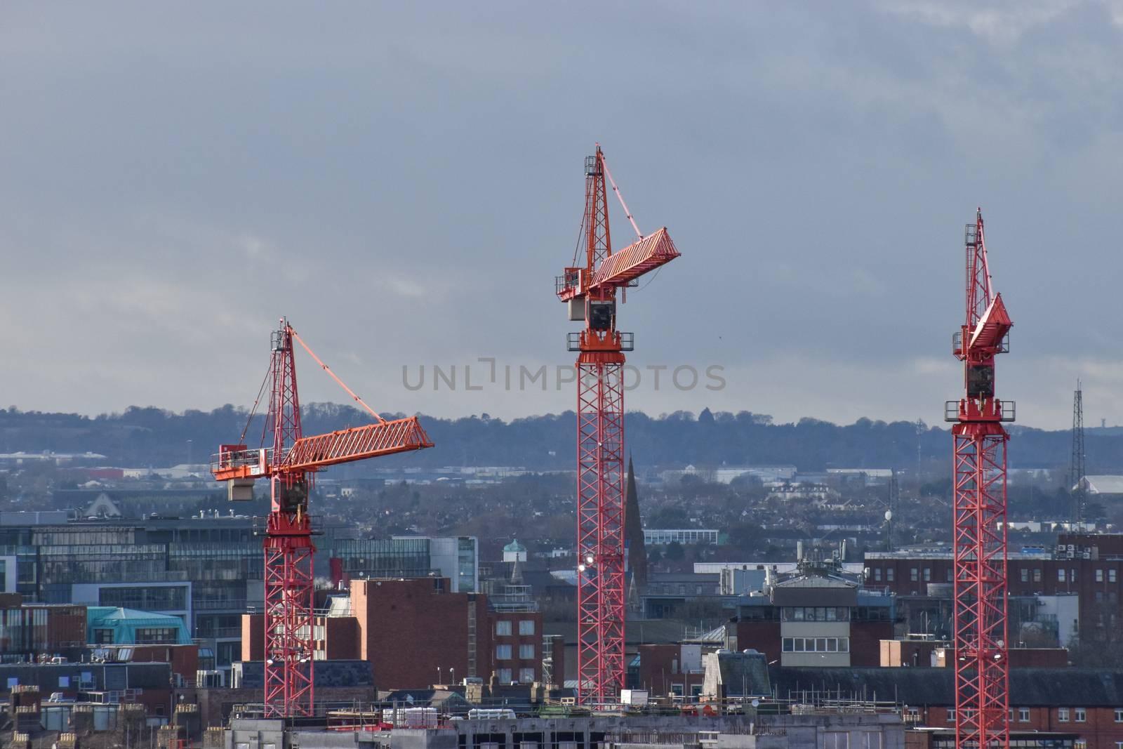 Three construction cranes set against a city skyline on a winters day