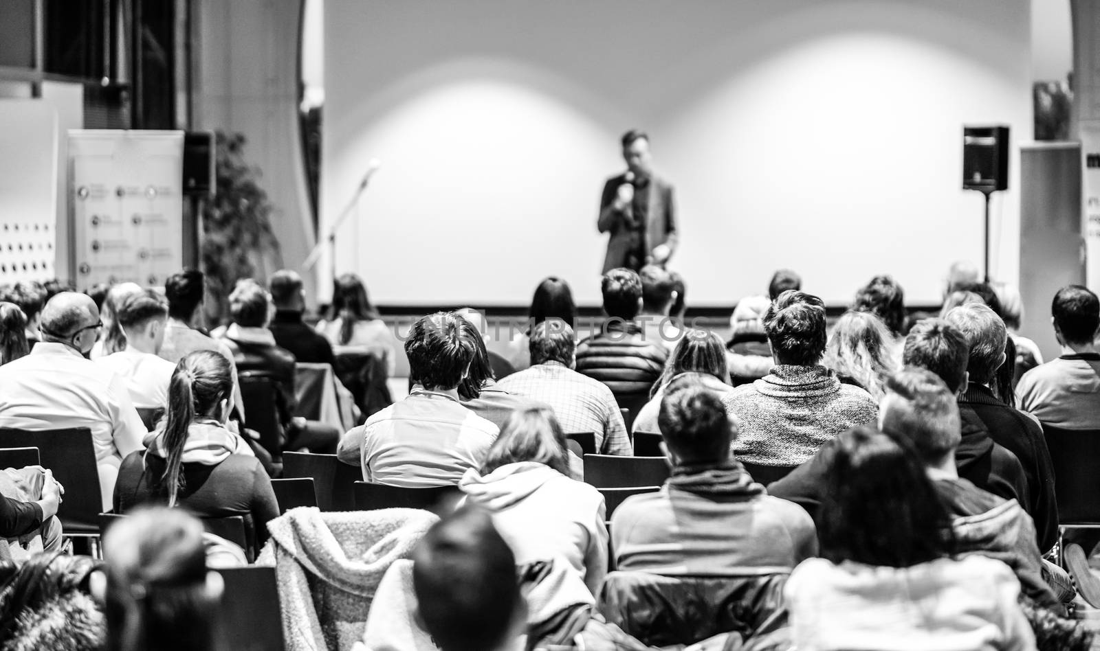 Speaker giving a talk in conference hall at business event. Audience at the conference hall. Business and Entrepreneurship concept. Focus on unrecognizable people in audience. Black and white image.