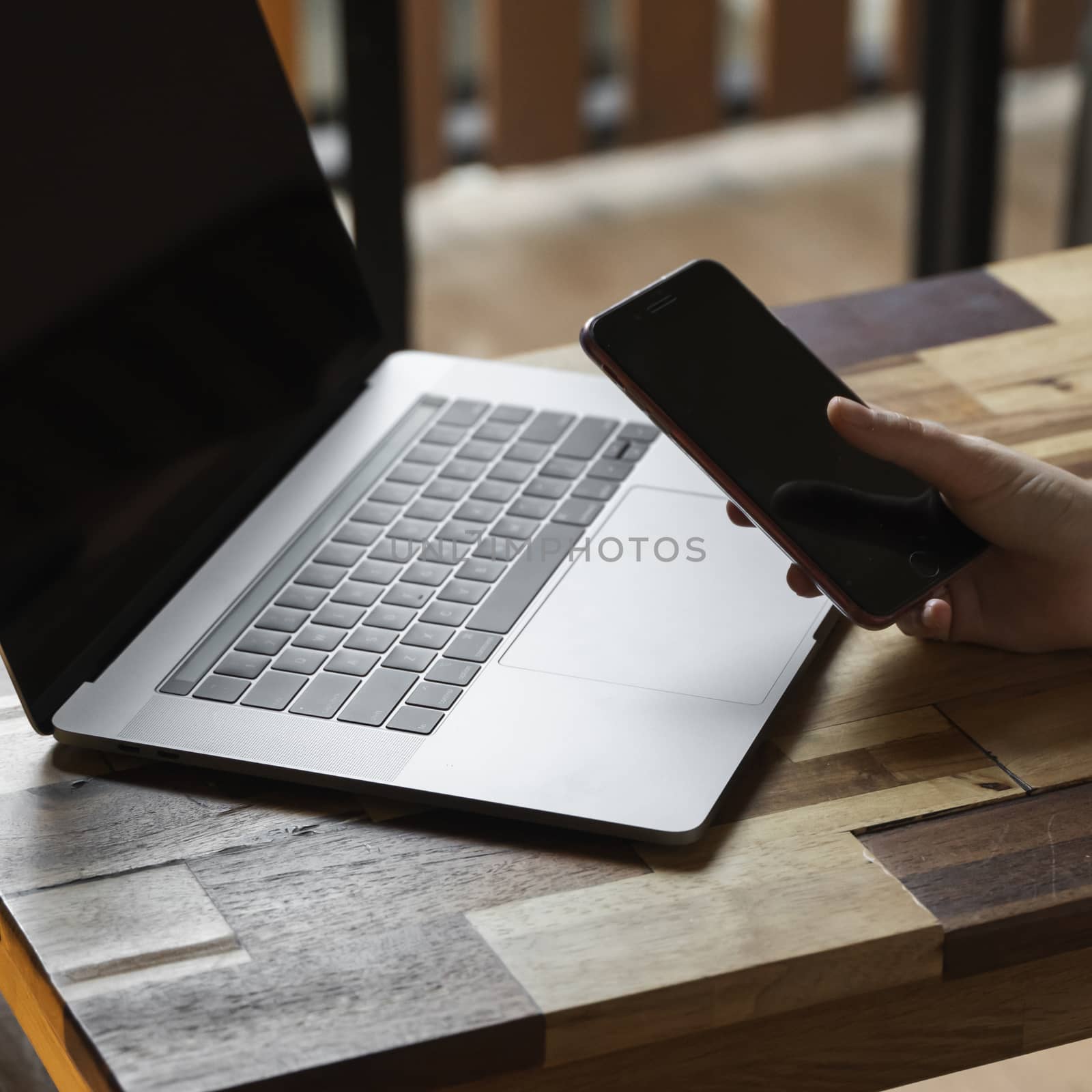 Woman's hands use a smartphone with a laptop. Study and work online, freelance. Self employed or freelance woman, girl working with her laptop sitting at wooden table with a phone and ereader