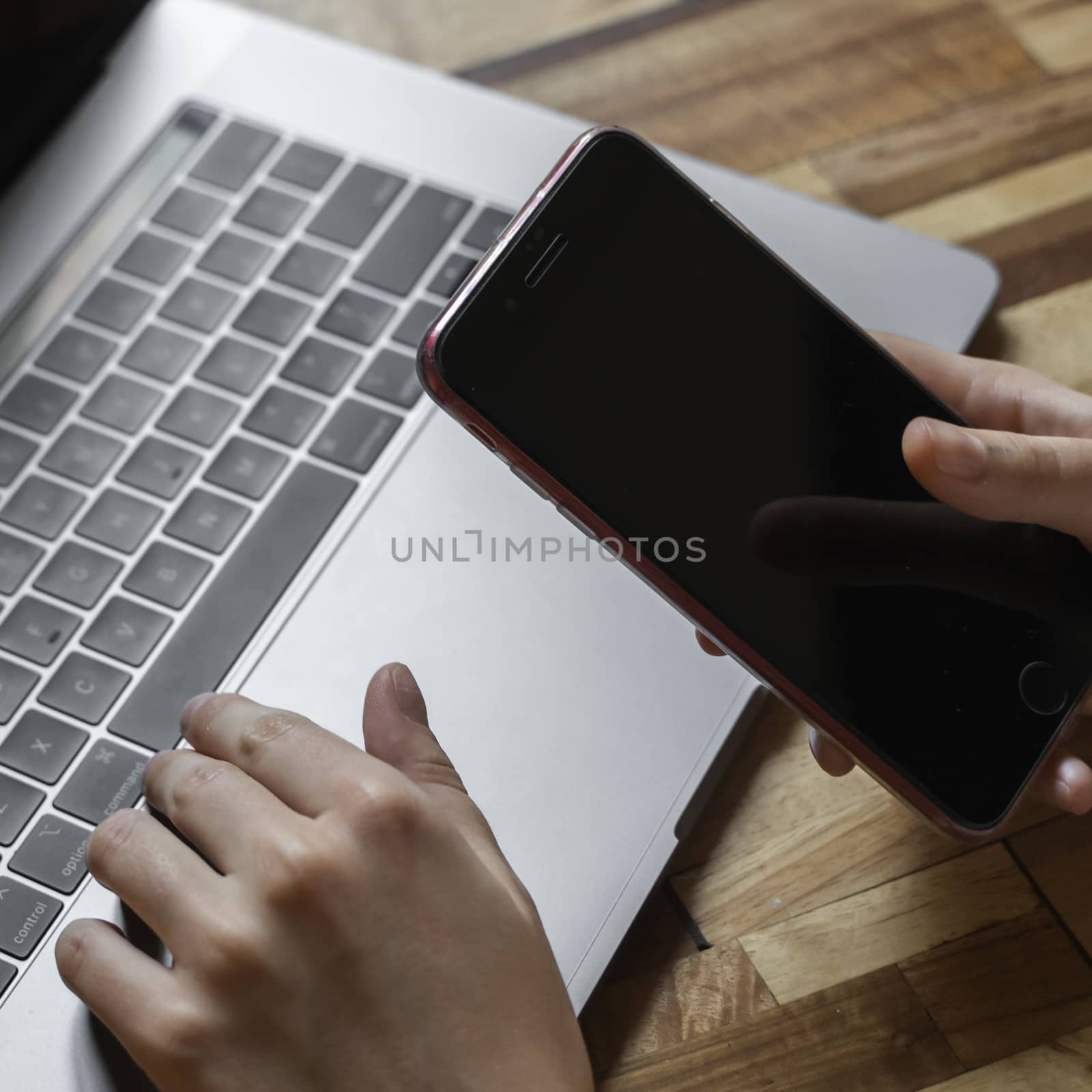 Woman's hands use a smartphone with a laptop. Study and work online, freelance. Self employed or freelance woman, girl working with her laptop sitting at wooden table with a phone and ereader. by vovsht