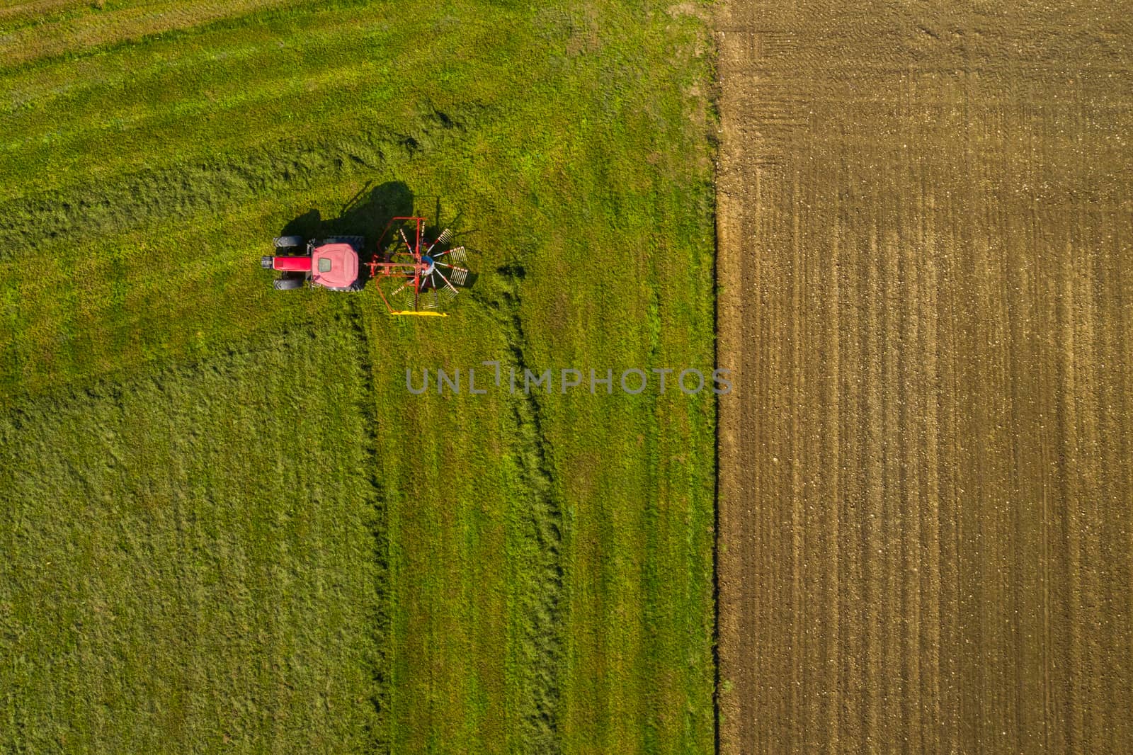 Top down aerial view of a red tractor cultivating farmland with a spinning rack by asafaric