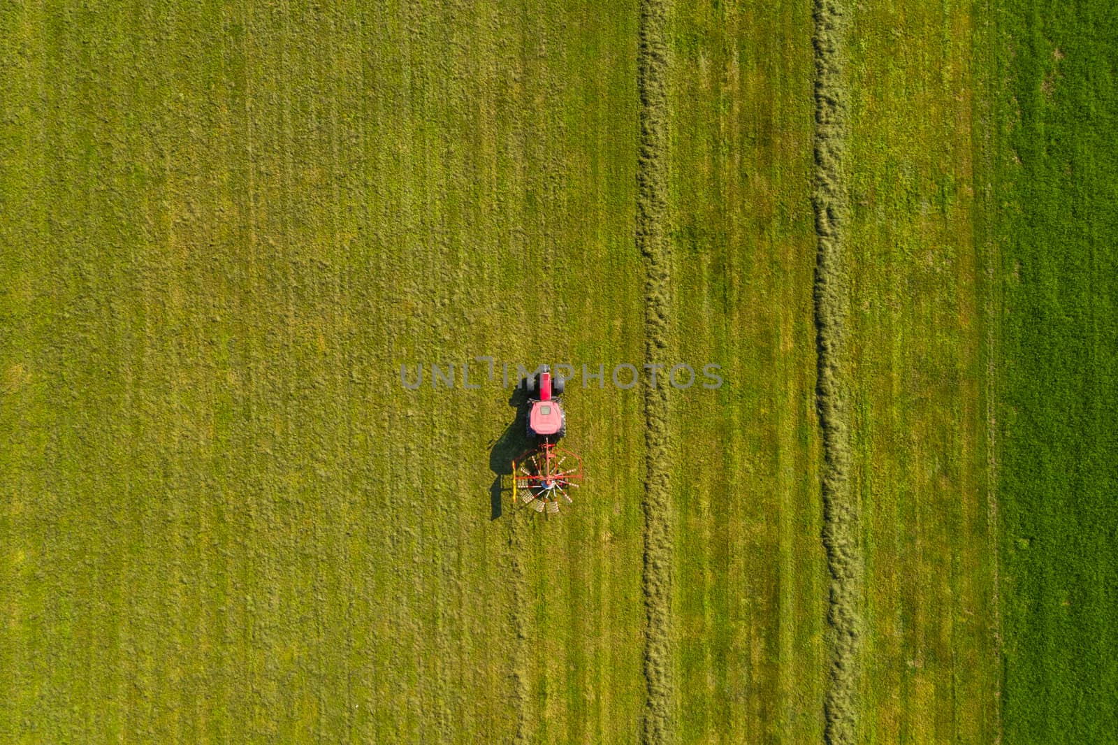 Top down aerial view of a red tractor cultivating farmland with a spinning rack by asafaric