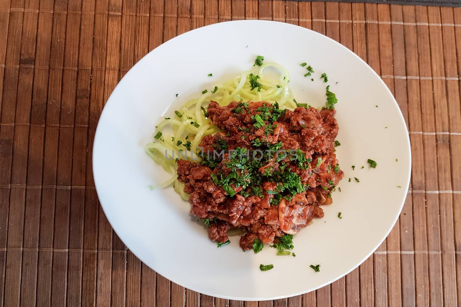 Healthy low carb food on white plate, lunch with snake cucumber in spaghetti strips cut above beef tartare with tomato sauce.