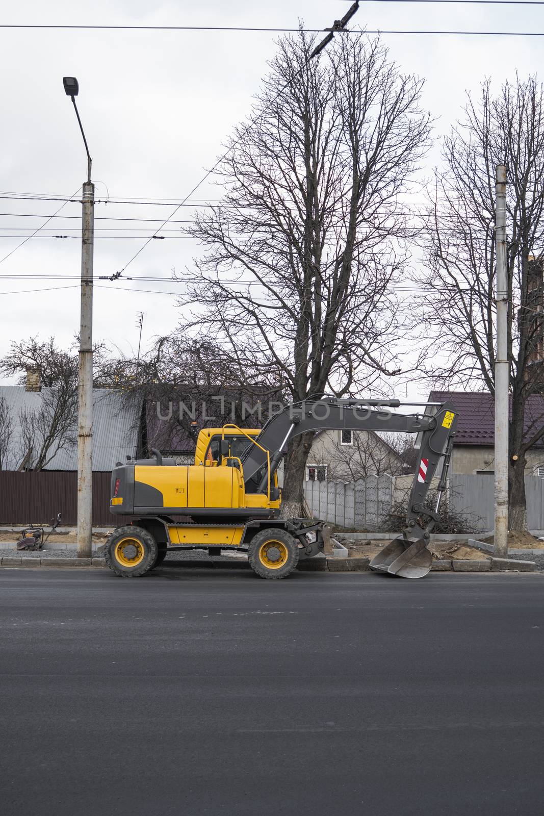 Yellow excavator standing on a road on construction site of the road on a street. Heavy industry. Construction of a road