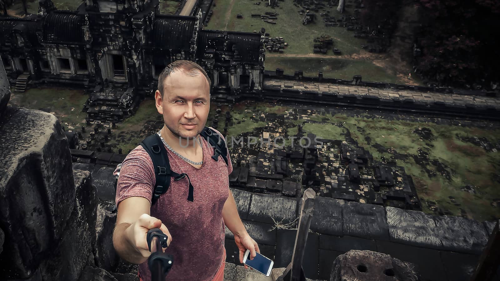 ANGKOR WAT, CAMBODIA. archaeological enclosure of Angkor Wat in Siam Reap. Young Caucasian adult man is making a selfie on the roof of the ancient temple in Asia. Green background. Copy space for text