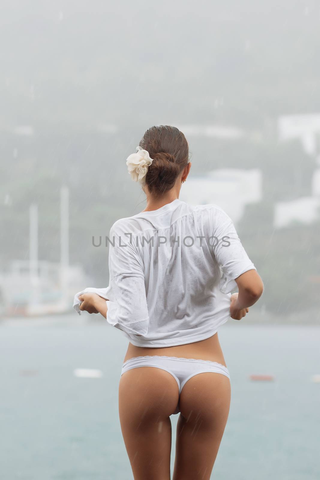 Back view of sensual female in white blouse and panties standing near sea on windy and rainy day