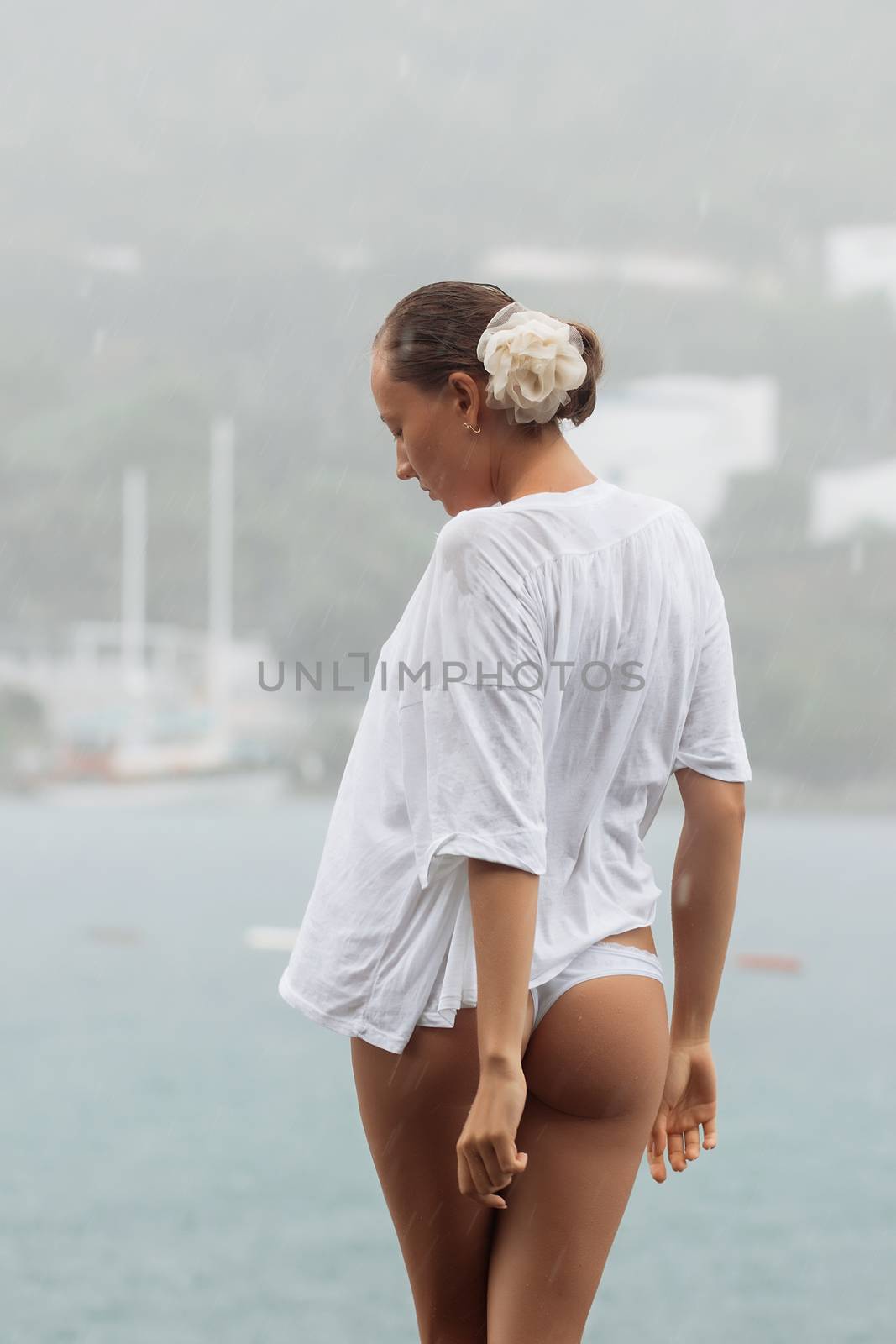 Back view of sensual female in white blouse and panties standing near sea on windy and rainy day
