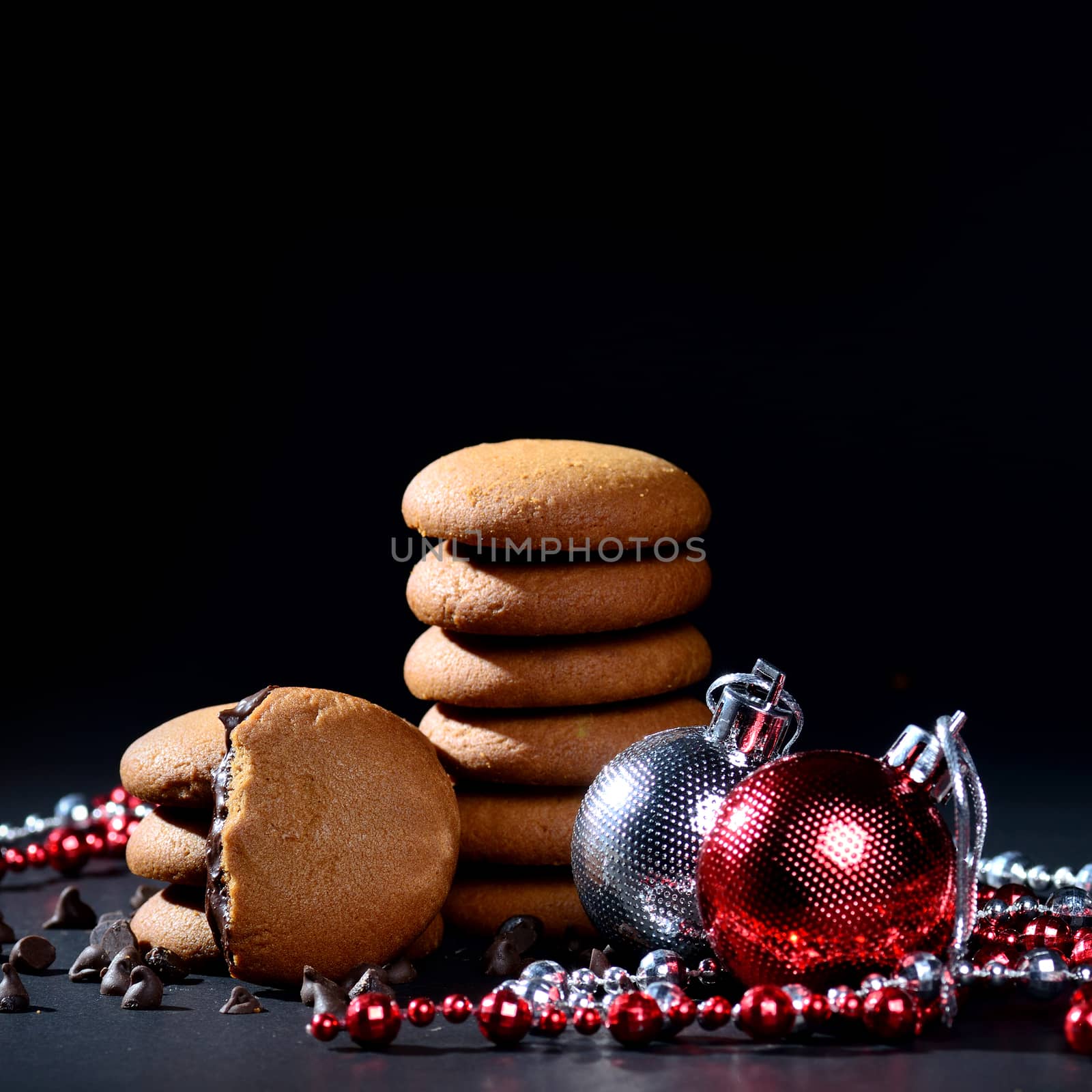 BISCUITS - Stack of delicious cream biscuits filled with chocolate cream decorated with Christmas Ornaments on black background