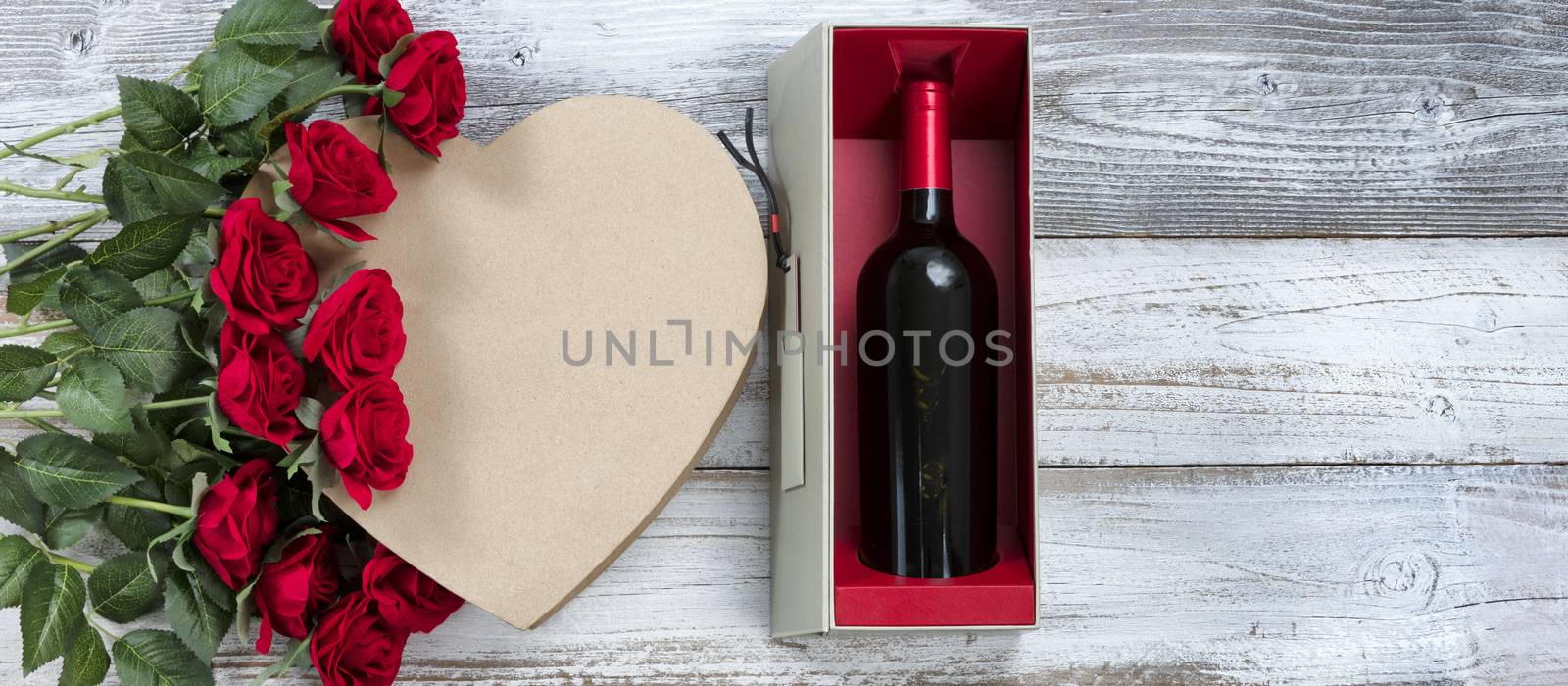 Happy Valentines Day celebration with wine, red roses and a heart shaped gift box on white rustic wood 