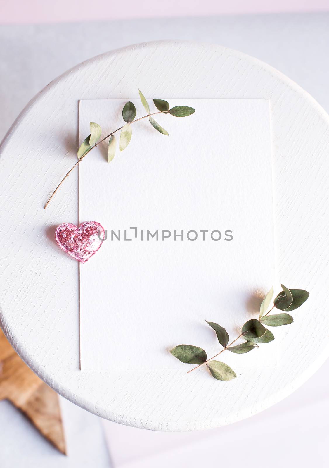 Background with copy space blank on table with glitter heart, eucalyptus branch, flowers and leafs. White paper top view, flat lay, minimal style. Moke up card