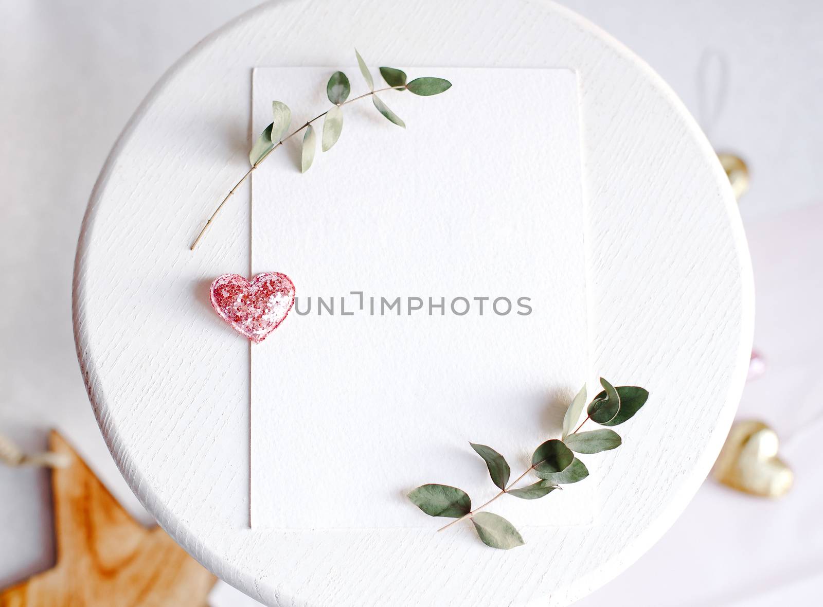 Background with copy space blank on table with glitter heart, eucalyptus branch, flowers and leafs. White paper top view, flat lay, minimal style. Moke up card