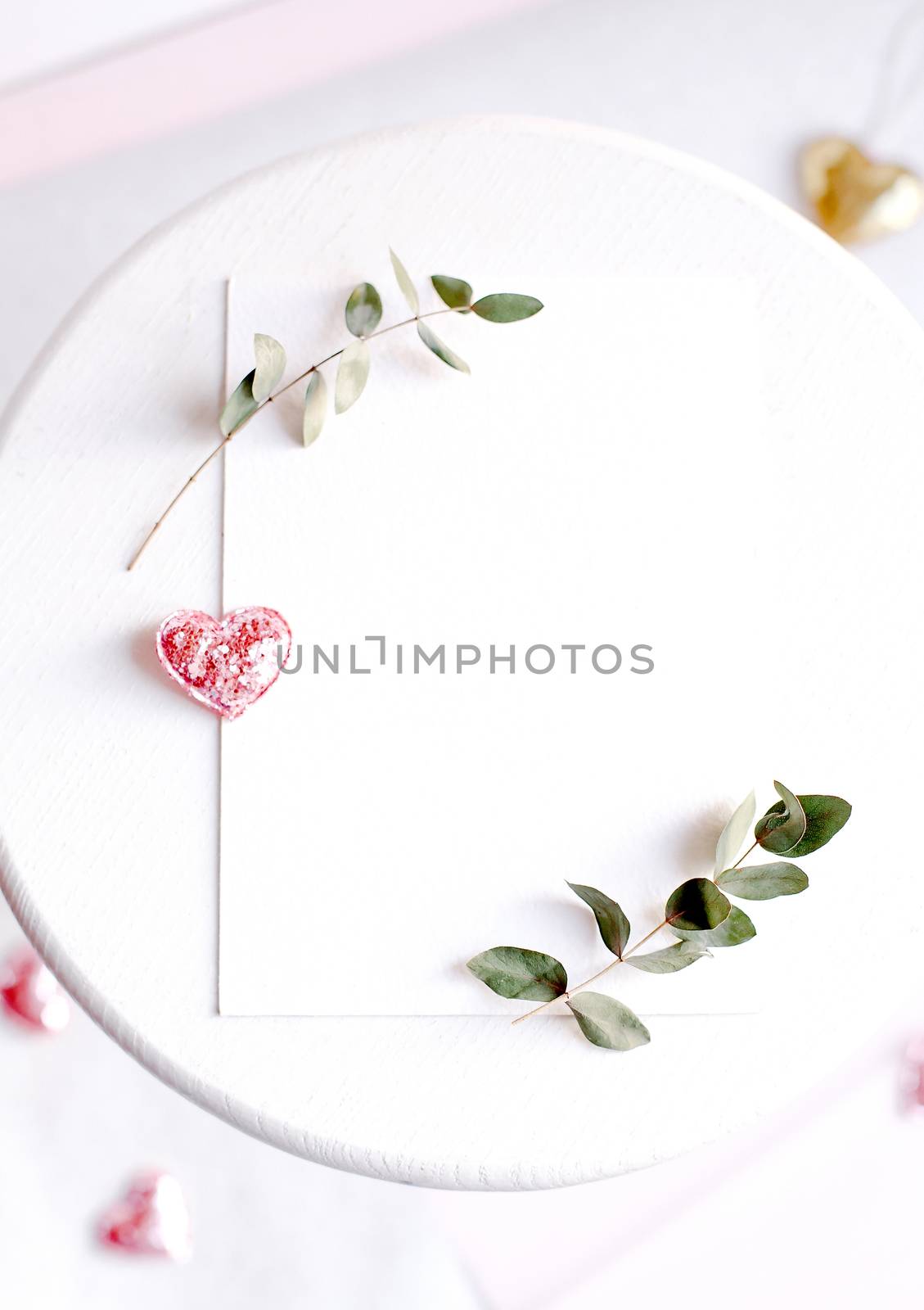 Background with copy space blank on table with glitter heart, eucalyptus branch, flowers and leafs. White paper top view, flat lay, minimal style. Moke up card