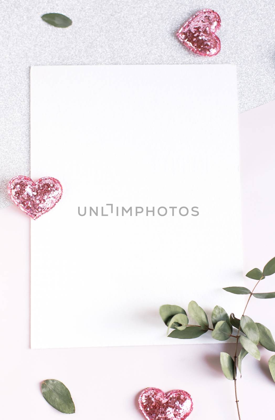 Background with copy space blank on table with glitter heart, eucalyptus branch, flowers and leafs. White paper top view, flat lay, minimal style. Moke up card