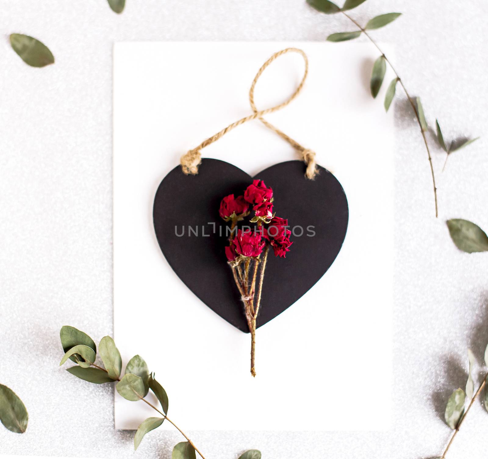 Background with copy space blank on table with black heart, eucalyptus branch, roses flowers and leafs. White paper top view, flat lay, minimal style. Moke up card