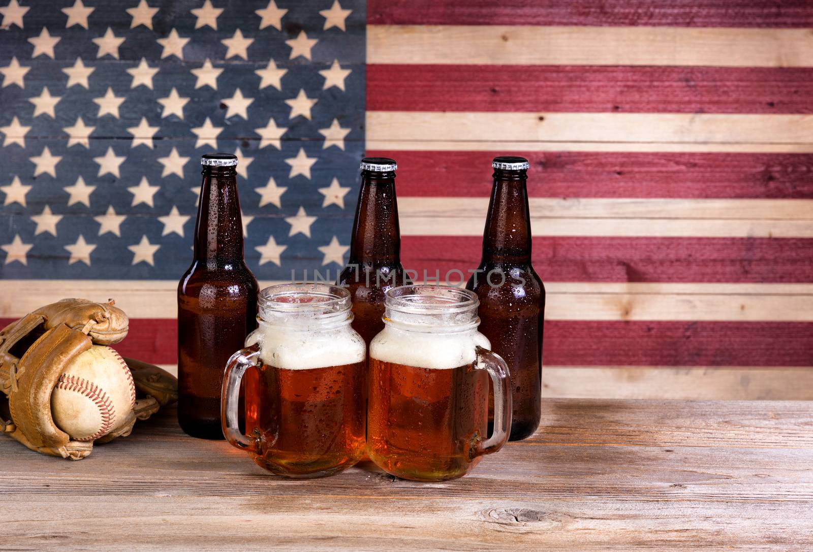 Two pint jars filled with beer, full bottles and baseball mitt with vintage wooden USA flag in background.