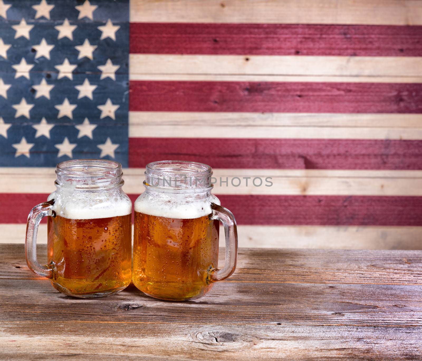 Two pint jars filled with beer with vintage wooden USA flag in background.