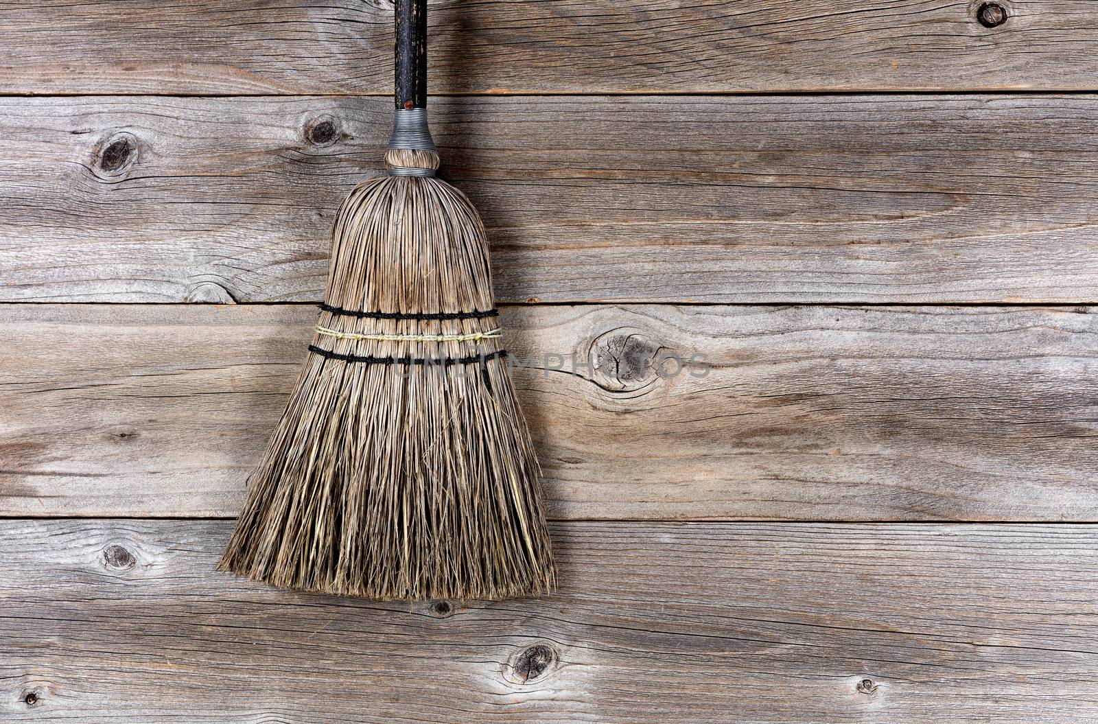 Old straw broom on stressed wooden floor. 