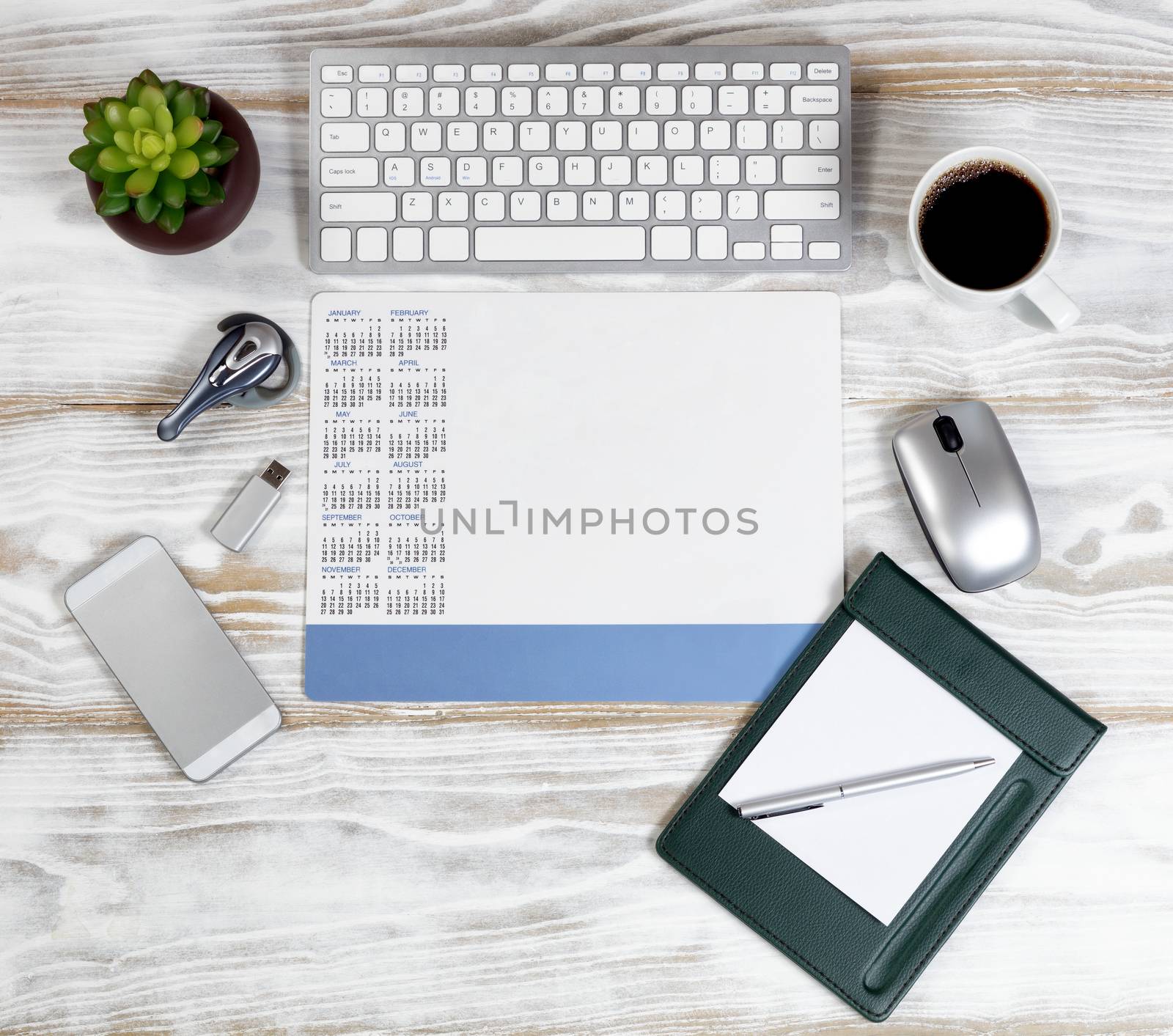 Overhead view of a modern technology devices with blank calendar on white wooden desktop 