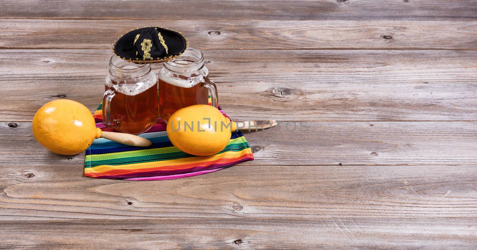 Cinco de Mayo concept with freshly poured beer, maracas, sombrero and placemat serapes on rustic table. 