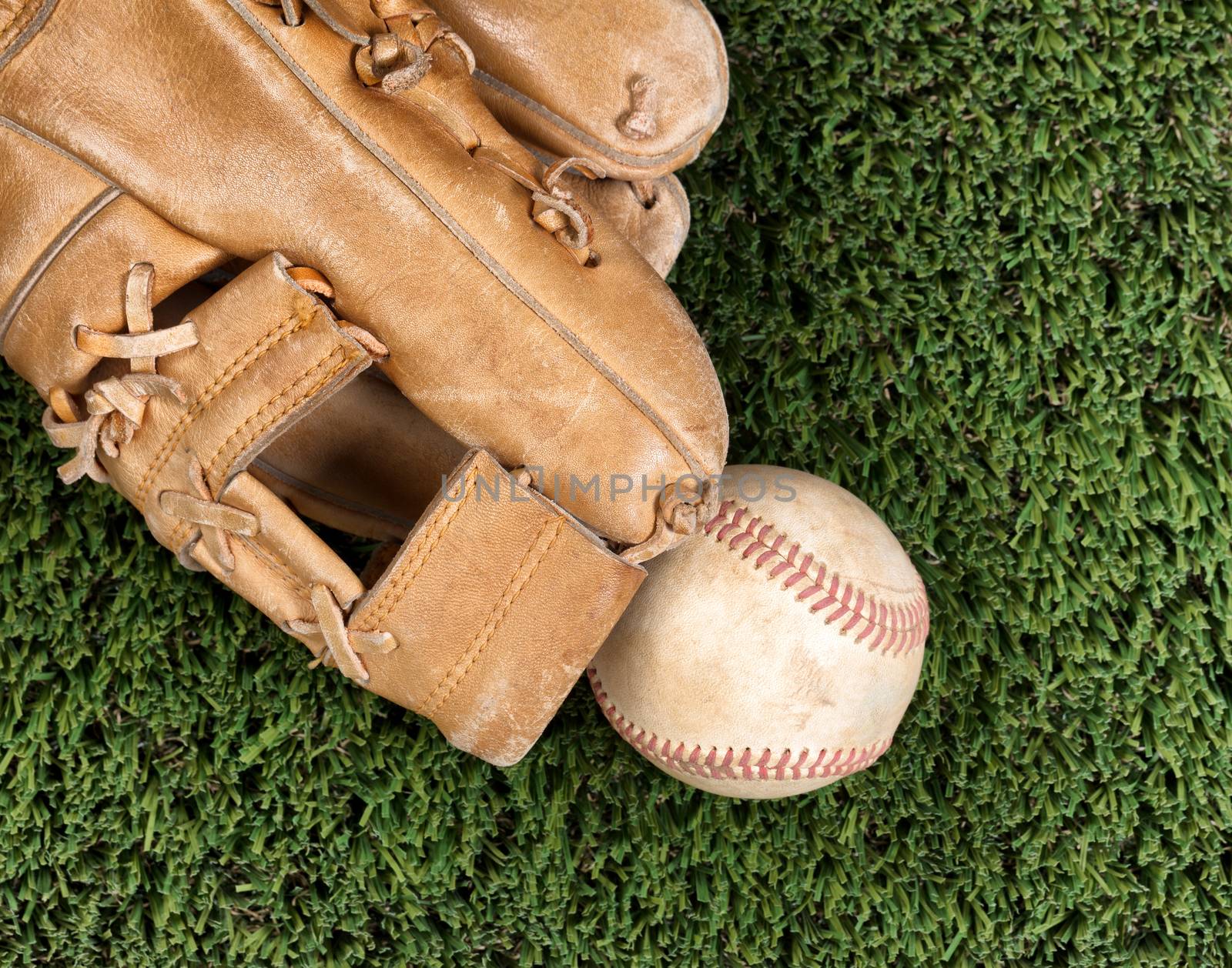 Flat view of old baseball mitt and used ball and on grass surface