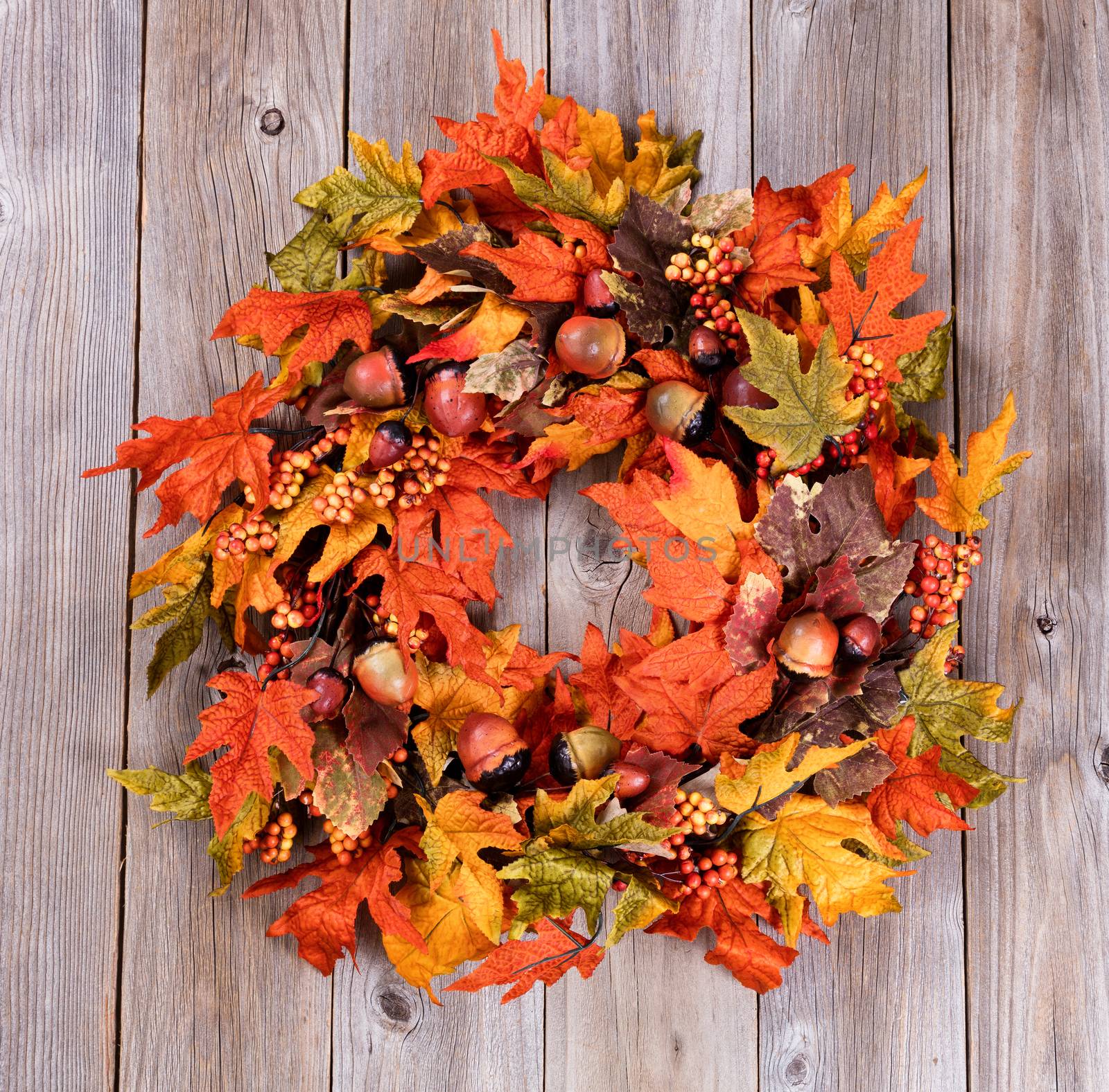 Overhead view of autumn wreath made with artificial leaves and acorns on rustic wood. 