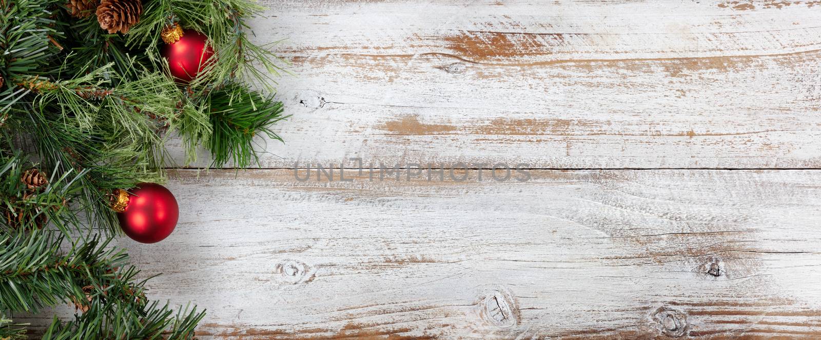 Rough fir branches with Christmas ball ornaments on rustic white wooden boards 