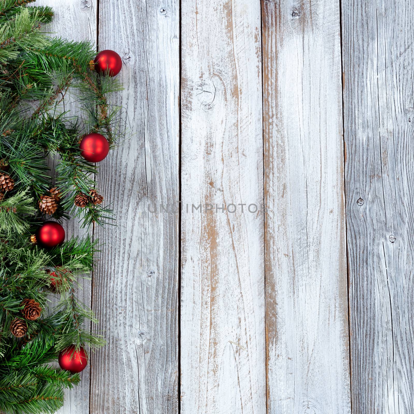 Christmas background with evergreen branches and red ornaments on white rustic wood 